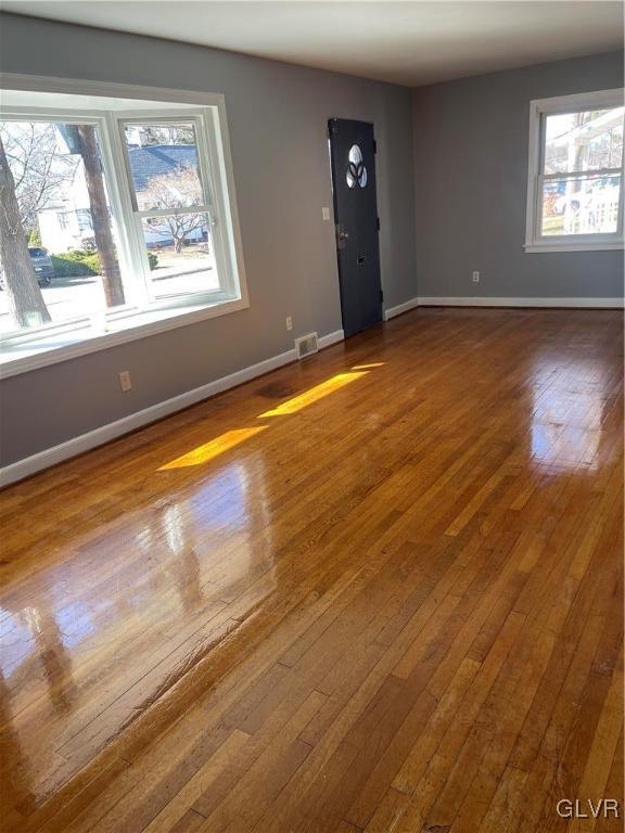 empty room with a wealth of natural light, wood-type flooring, visible vents, and baseboards