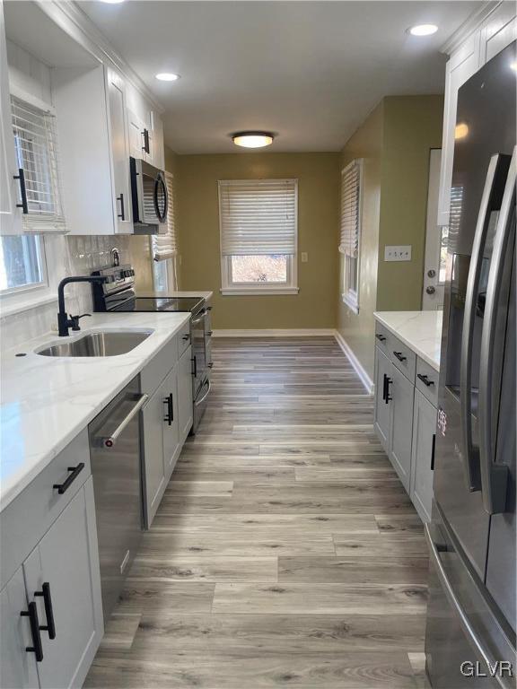 kitchen with backsplash, appliances with stainless steel finishes, light wood-style floors, a sink, and light stone countertops