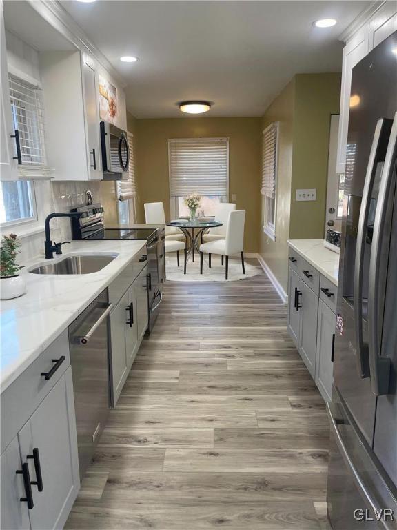 kitchen featuring appliances with stainless steel finishes, light wood-style floors, a sink, and light stone countertops