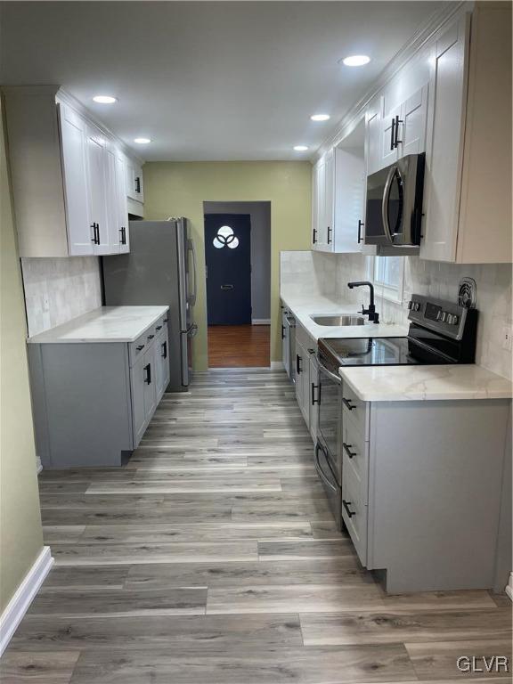 kitchen featuring tasteful backsplash, light wood-style flooring, stainless steel appliances, light countertops, and a sink