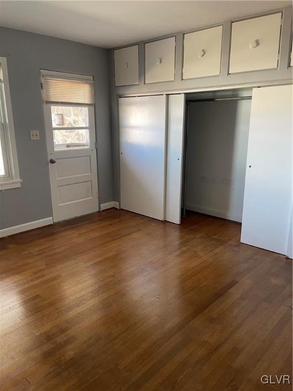 unfurnished bedroom featuring dark wood-style flooring, a closet, and baseboards