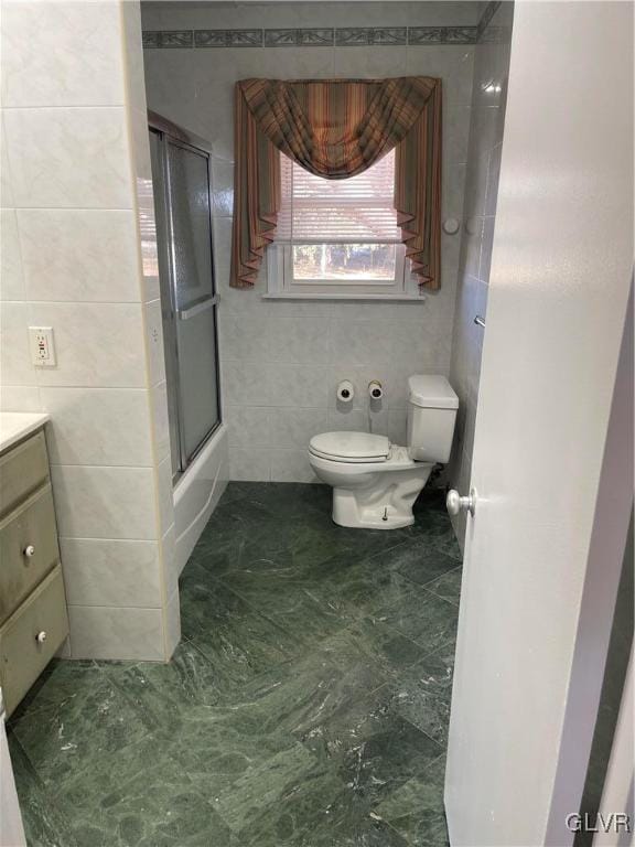 bathroom with toilet, shower / bath combination with glass door, tile walls, and vanity