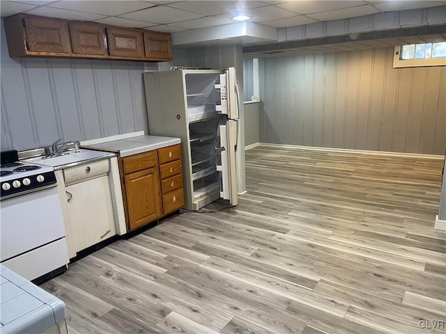 kitchen featuring tile counters, brown cabinetry, light wood-style floors, white appliances, and a drop ceiling