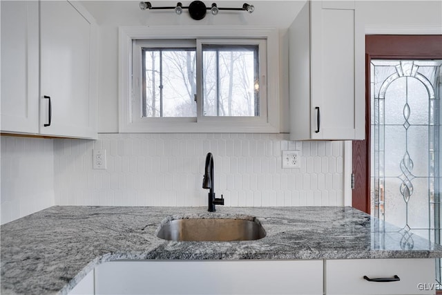 kitchen featuring light stone counters, white cabinets, a sink, and decorative backsplash