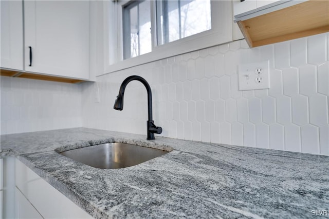 room details featuring light stone counters, white cabinets, and a sink