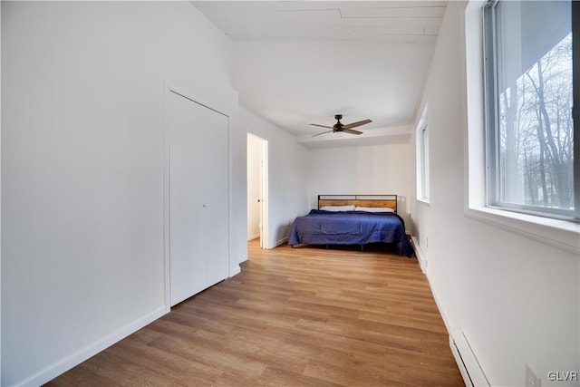 unfurnished bedroom featuring ceiling fan, baseboard heating, light wood-style flooring, and baseboards