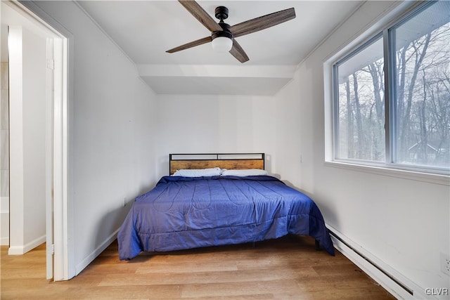 bedroom featuring baseboard heating, light wood-type flooring, a ceiling fan, and baseboards