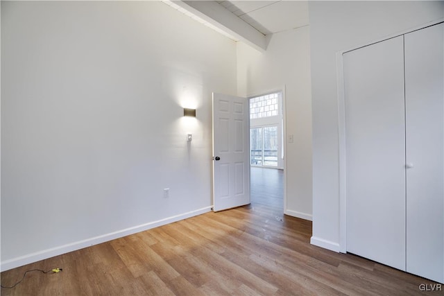 unfurnished bedroom with a high ceiling, beamed ceiling, wood finished floors, and baseboards