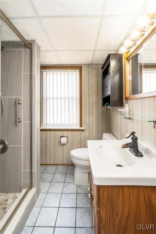 full bath with toilet, a shower stall, vanity, a drop ceiling, and tile patterned floors