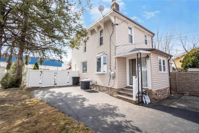 view of front of property featuring entry steps, a chimney, a gate, fence, and central AC