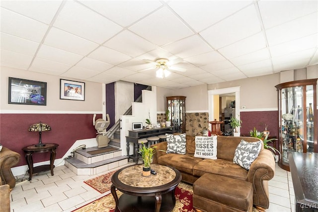 living room featuring a ceiling fan, tile patterned flooring, a drop ceiling, and stairway