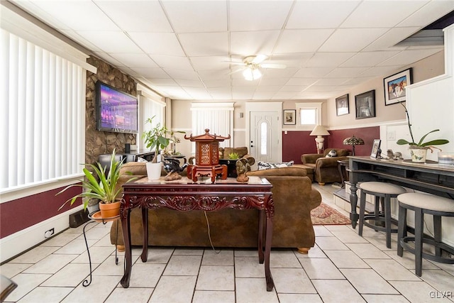 living area with a ceiling fan, a paneled ceiling, and light tile patterned floors