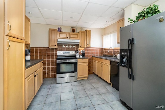 kitchen with dark countertops, a paneled ceiling, appliances with stainless steel finishes, a sink, and under cabinet range hood