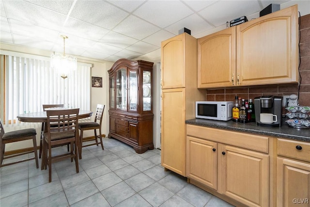 kitchen with dark countertops, a paneled ceiling, backsplash, light brown cabinetry, and white microwave