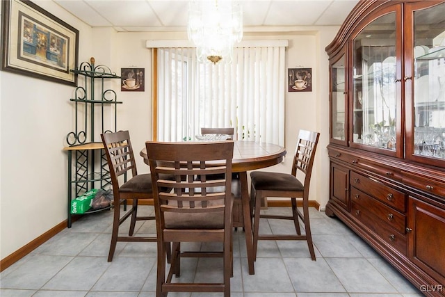 dining area with light tile patterned flooring, a notable chandelier, a drop ceiling, and baseboards