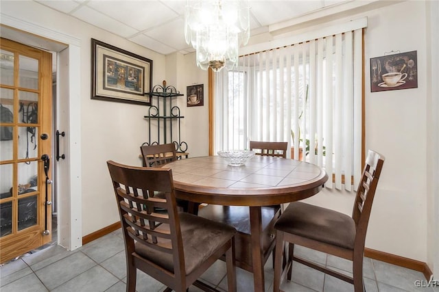 dining area featuring tile patterned flooring, a drop ceiling, a notable chandelier, and baseboards