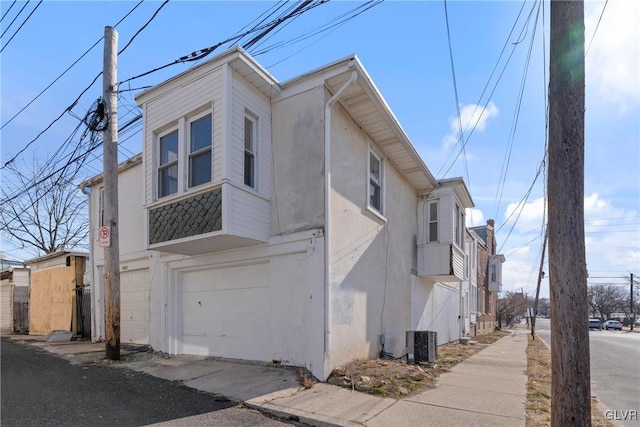 view of side of property featuring a garage, central air condition unit, and stucco siding