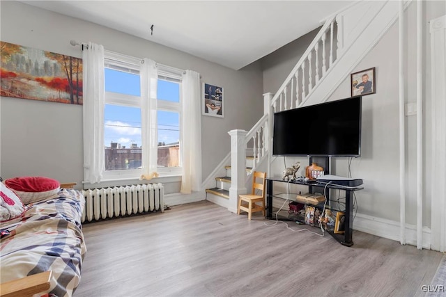 living area with radiator, baseboards, stairway, and wood finished floors