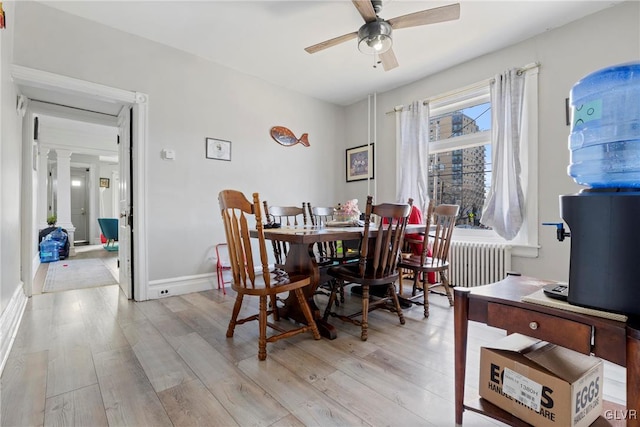 dining room with a ceiling fan, baseboards, light wood-type flooring, radiator heating unit, and ornate columns