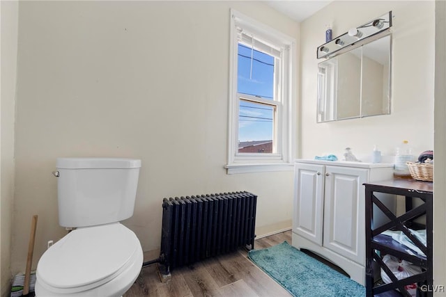 half bath with radiator, toilet, wood finished floors, and vanity