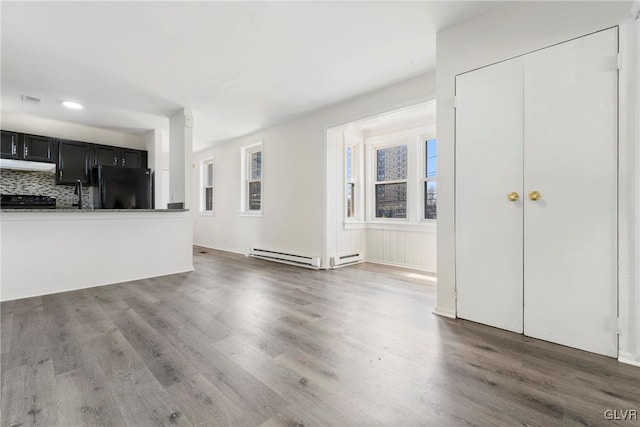 unfurnished living room with visible vents, baseboard heating, and wood finished floors