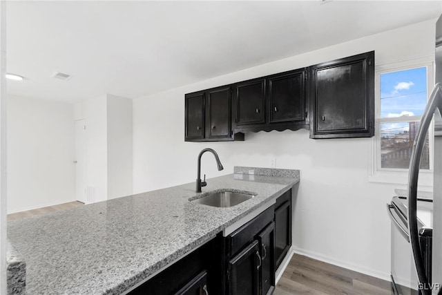 kitchen featuring light stone counters, light wood-style flooring, dark cabinets, a sink, and visible vents