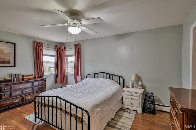 bedroom with a baseboard heating unit, wood finished floors, and a ceiling fan