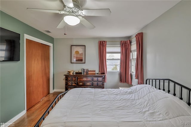 bedroom with a closet, wood finished floors, visible vents, and baseboards