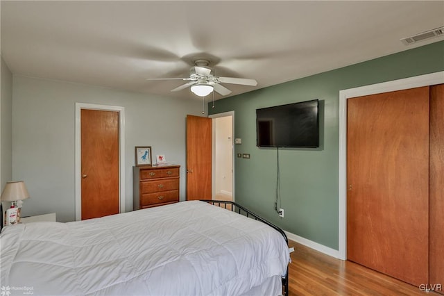 bedroom featuring ceiling fan, wood finished floors, visible vents, baseboards, and a closet