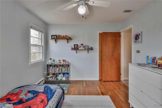 bedroom with ceiling fan, light wood-style flooring, a baseboard heating unit, visible vents, and baseboards