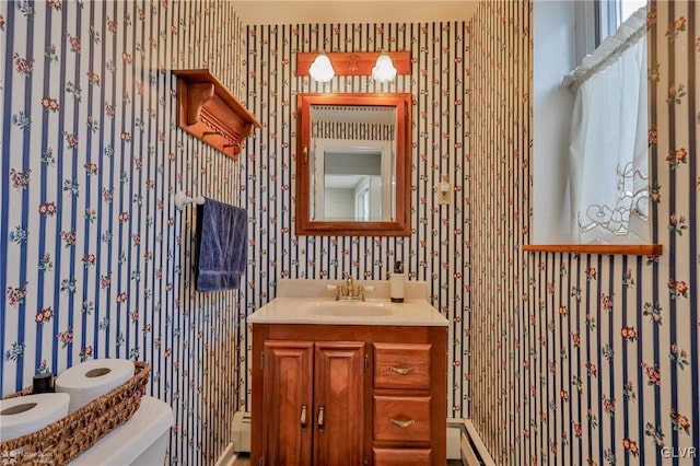 half bathroom with a baseboard radiator, vanity, toilet, and wallpapered walls