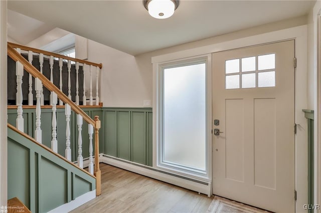 entrance foyer with a decorative wall, light wood-style floors, stairs, baseboard heating, and wainscoting