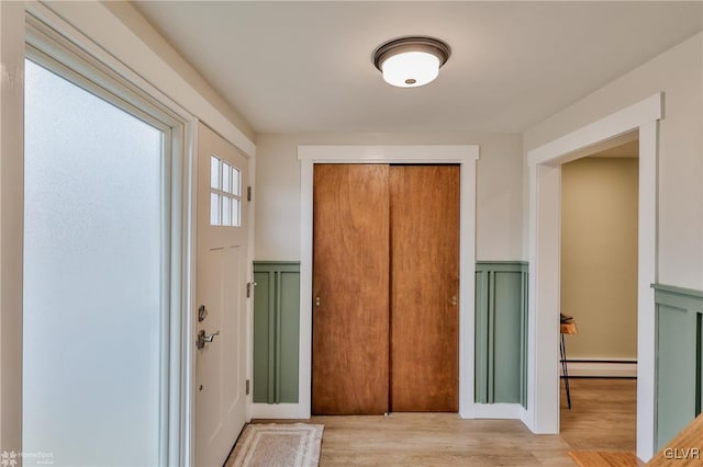 foyer entrance with wainscoting, a decorative wall, baseboard heating, and wood finished floors