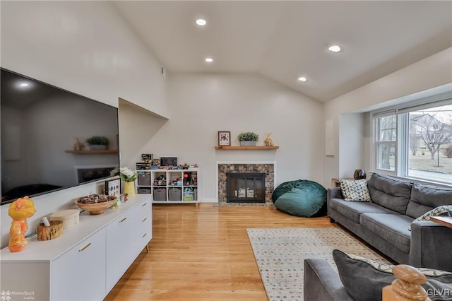 living area with lofted ceiling, a stone fireplace, recessed lighting, and light wood-style floors