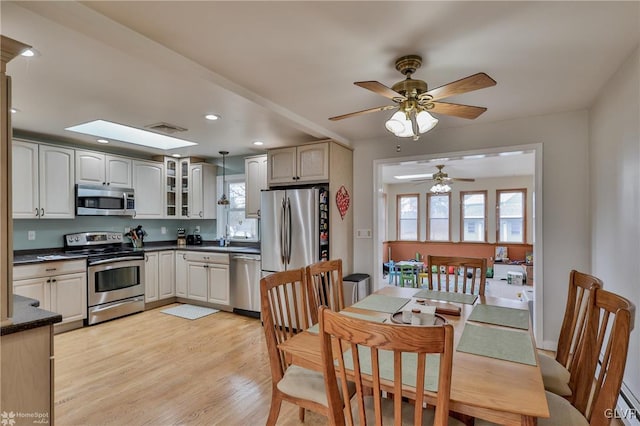 kitchen with a skylight, dark countertops, appliances with stainless steel finishes, glass insert cabinets, and light wood-type flooring