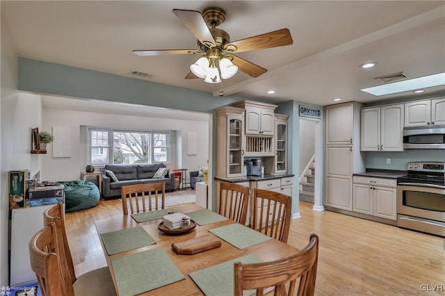 dining space featuring stairs, light wood-style flooring, a skylight, and visible vents