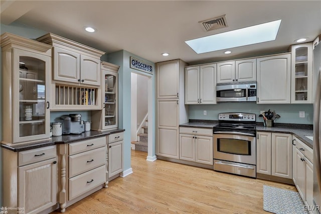 kitchen featuring stainless steel appliances, dark countertops, visible vents, light wood-style floors, and glass insert cabinets