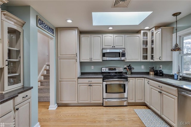 kitchen featuring a skylight, stainless steel appliances, visible vents, glass insert cabinets, and a sink