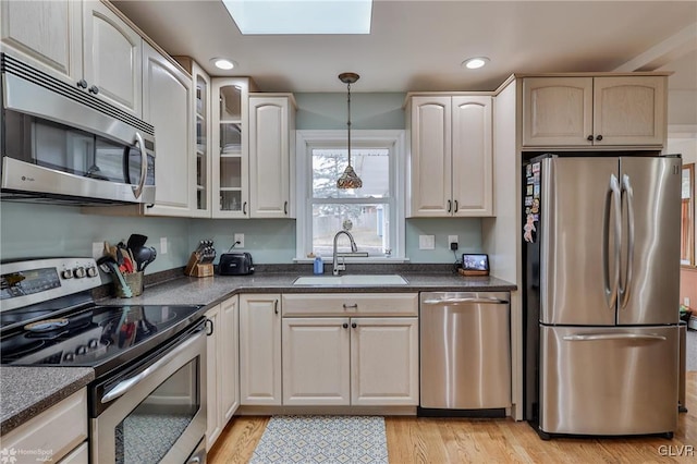 kitchen with dark countertops, appliances with stainless steel finishes, hanging light fixtures, light wood-type flooring, and a sink