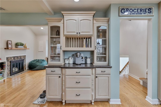 bar featuring light wood finished floors, beamed ceiling, a fireplace with flush hearth, and baseboards