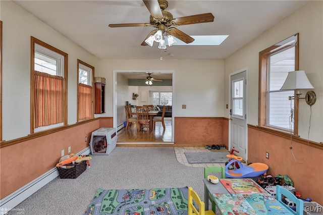 playroom with ceiling fan, a baseboard radiator, a wainscoted wall, a baseboard heating unit, and carpet flooring