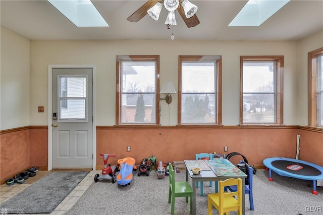 recreation room with a ceiling fan, a skylight, carpet flooring, and tile patterned floors