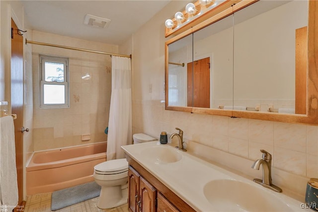 bathroom featuring toilet, tile walls, shower / bath combo with shower curtain, and a sink