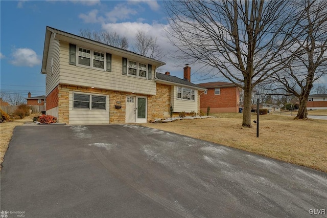 split level home with stone siding, a chimney, aphalt driveway, and a front yard