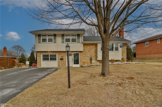 tri-level home featuring aphalt driveway, stone siding, a chimney, and a garage