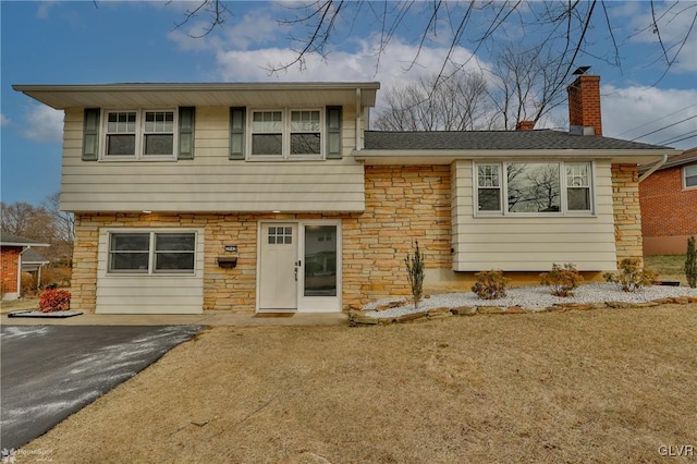 split level home with stone siding, aphalt driveway, and a chimney