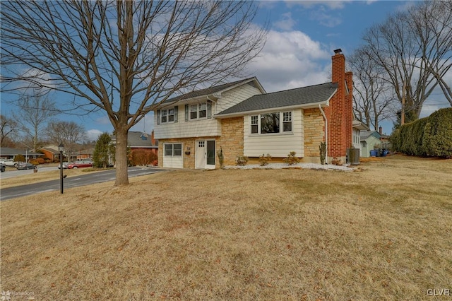 tri-level home with aphalt driveway, a chimney, central air condition unit, stone siding, and a front lawn