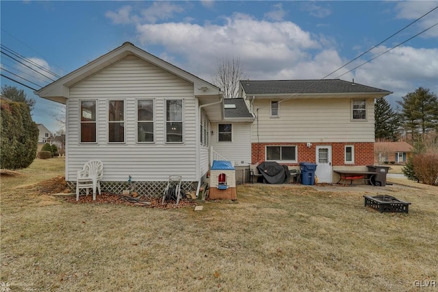 back of property featuring brick siding, an outdoor fire pit, and a yard