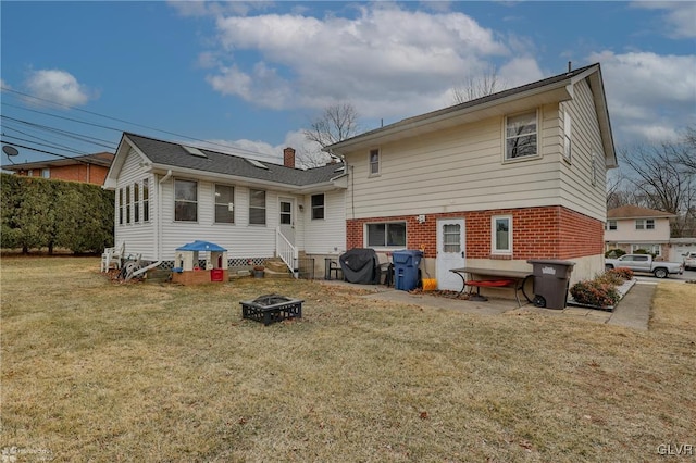 back of house with entry steps, a fire pit, brick siding, a lawn, and a chimney