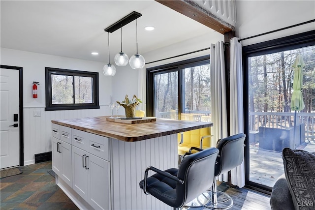 kitchen with stone finish flooring, decorative light fixtures, butcher block counters, a breakfast bar area, and white cabinets